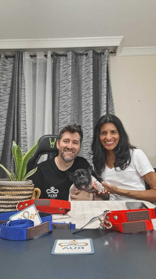 Familia detrás de Rúa Infinity: pareja sonriente junto a su perro, con collares y accesorios para perros sobre la mesa.